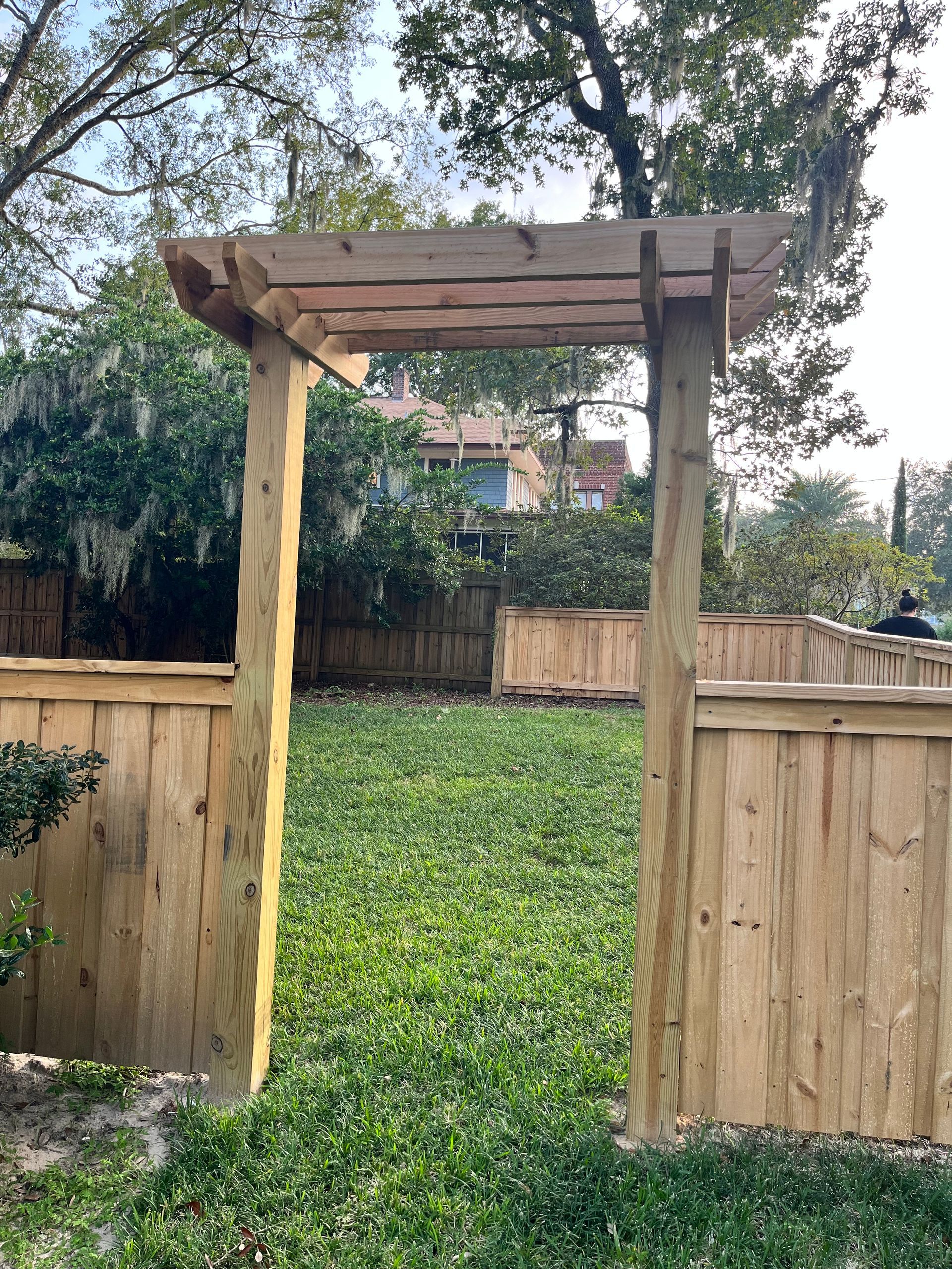 A wooden pergola is sitting on top of a wooden fence in a backyard.