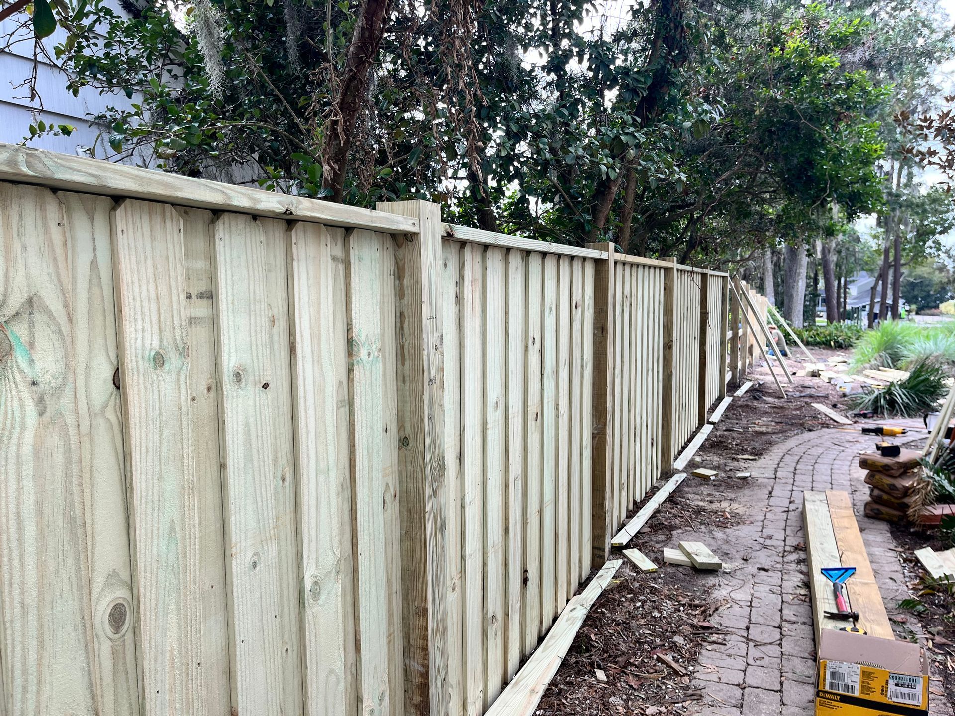 A wooden fence is being built next to a brick walkway.