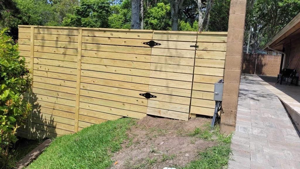 A wooden fence is surrounded by grass and trees in a backyard.