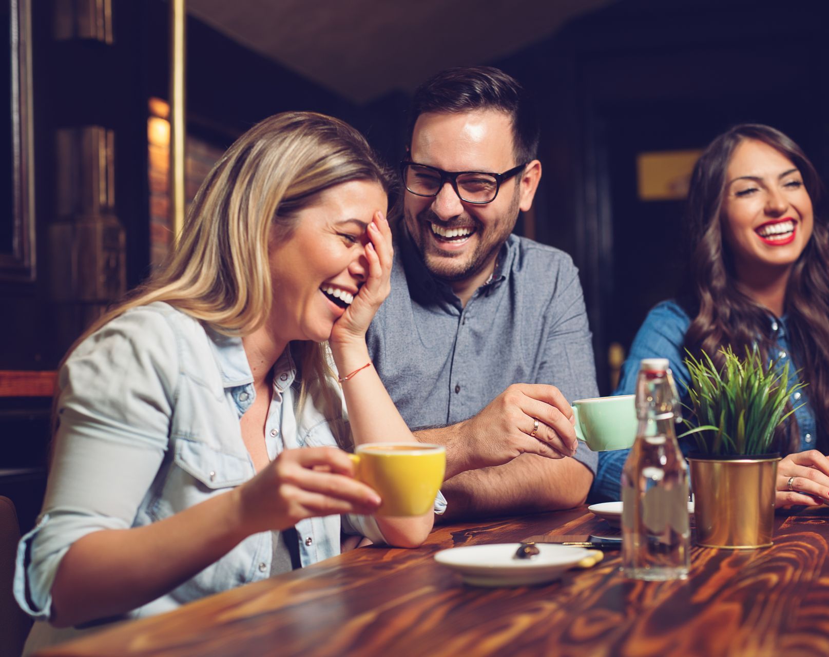 A group of people are sitting at a table laughing and drinking coffee.