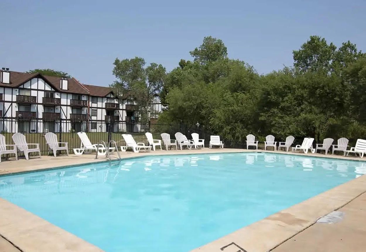 A large swimming pool with chairs around it in front of a building