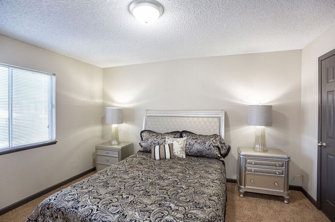 A bedroom with a bed , nightstands , lamps and a window.