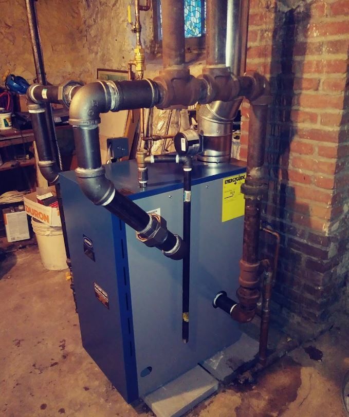 A boiler is sitting in a basement next to a brick wall