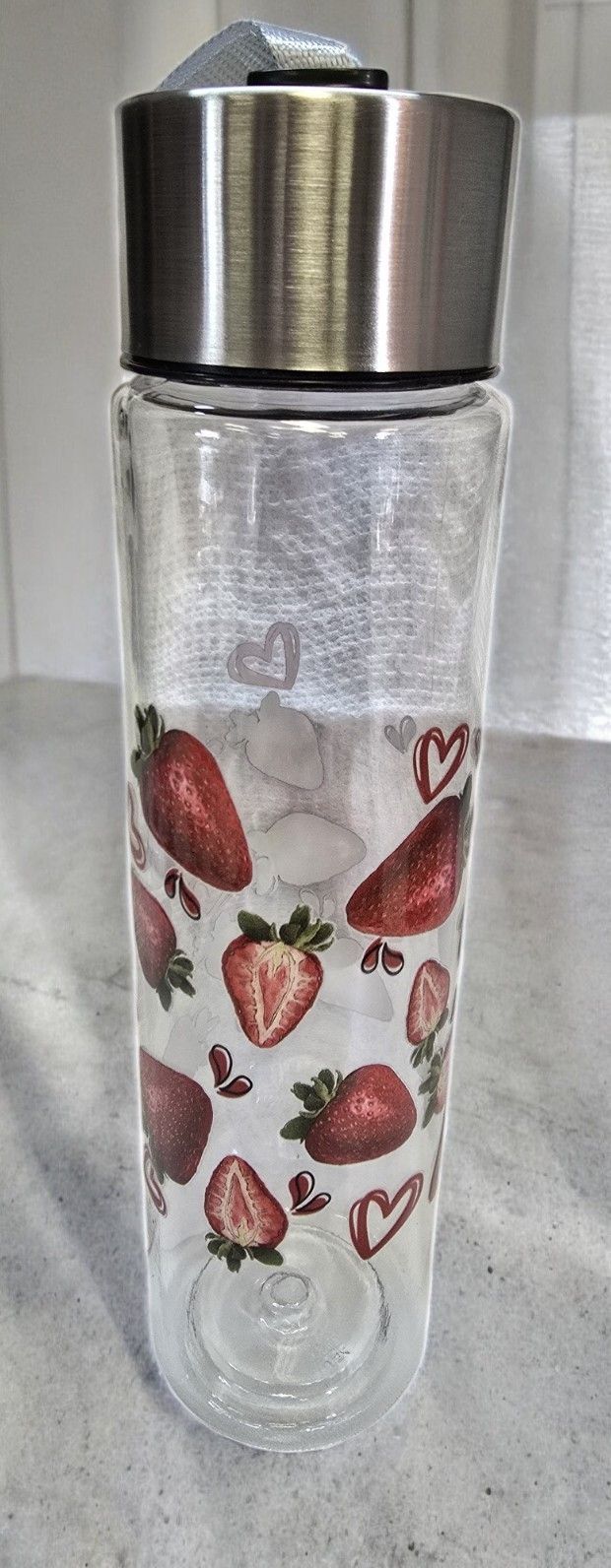 A glass water bottle with strawberries on it is sitting on a table.