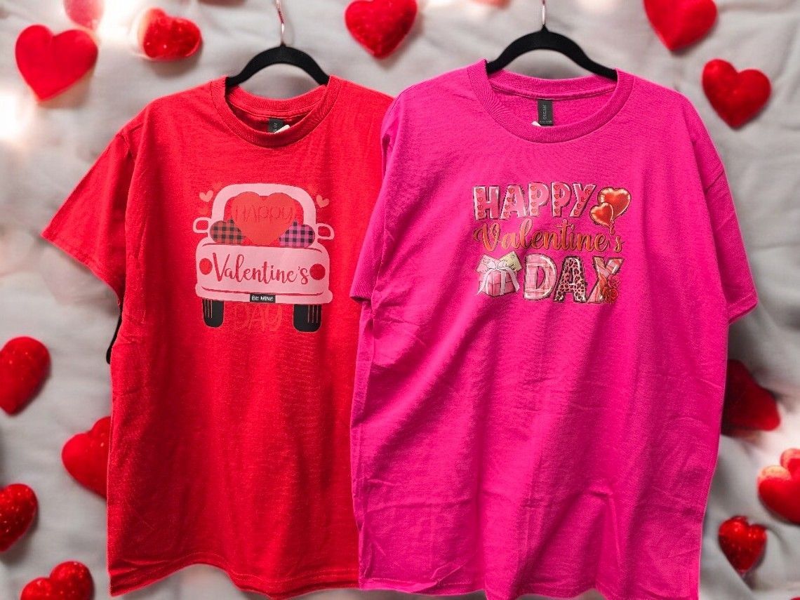 Two t-shirts are hanging on a hanger with hearts in the background.