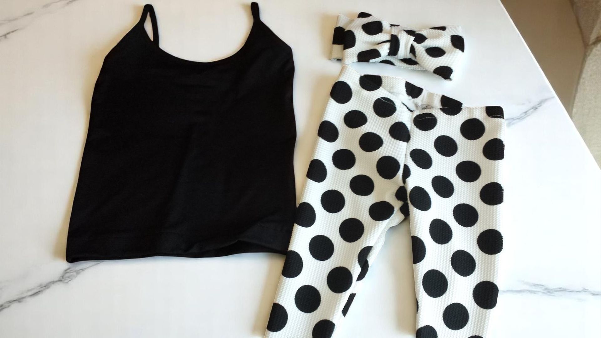 A black tank top and polka dot pants are on a table.