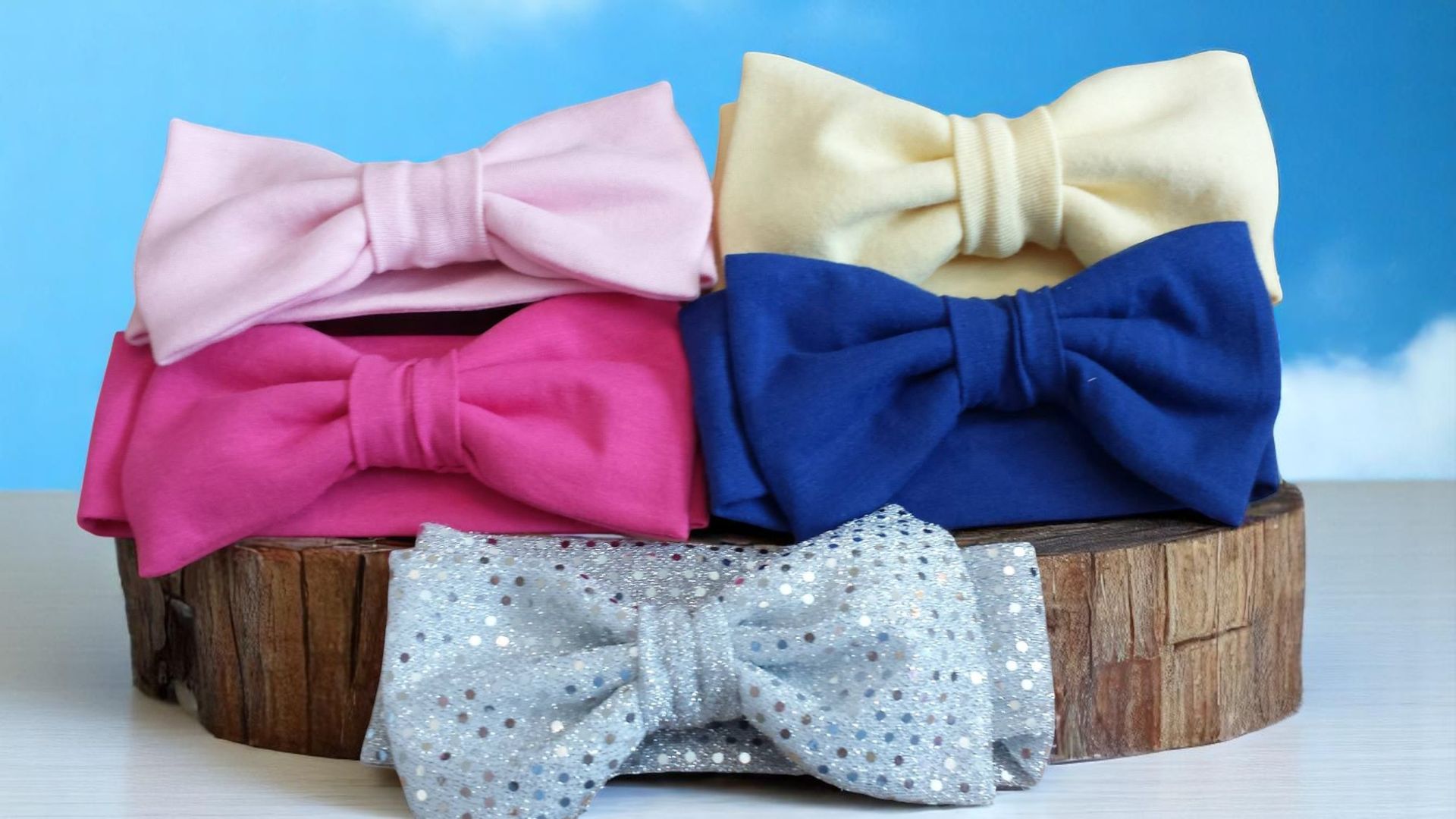 Four different colored bow ties are stacked on top of each other on a wooden stump.