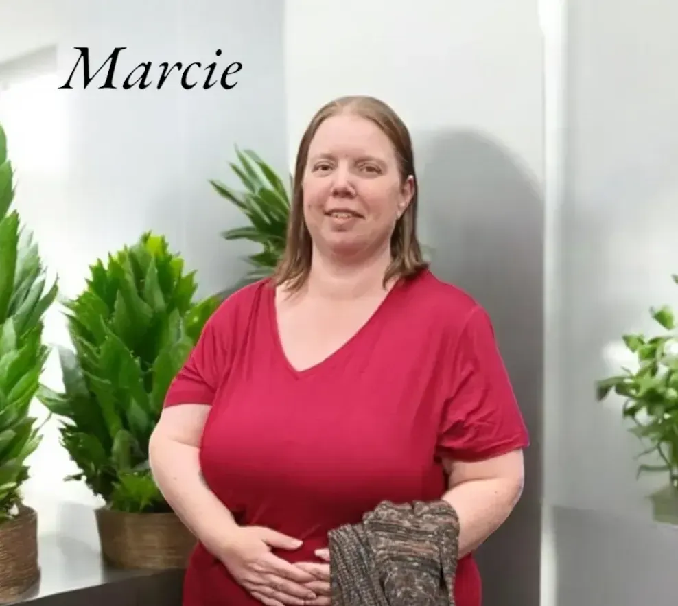 A woman in a red shirt is standing in front of a wall with the name marcie on it