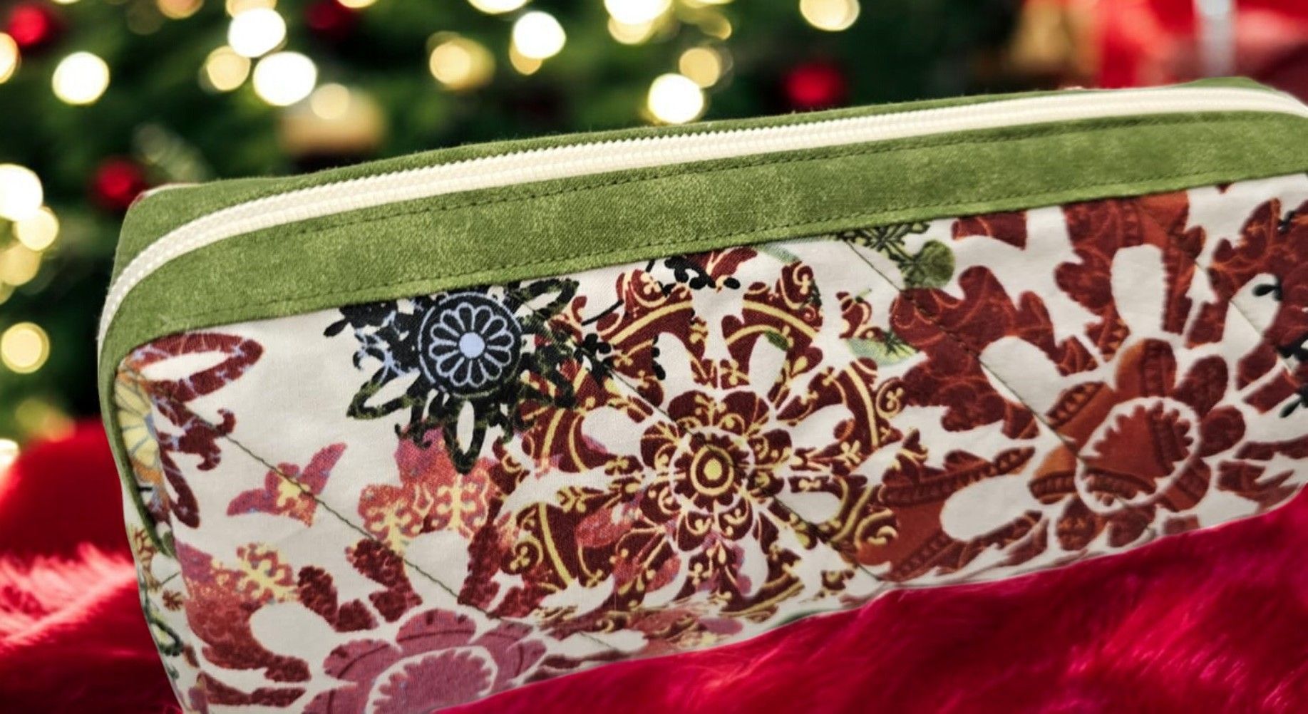 A pencil case with a floral pattern is sitting on a red blanket in front of a christmas tree.