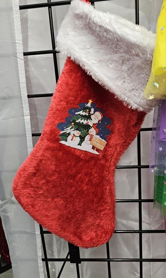 A red christmas stocking with a snowman and a christmas tree on it is hanging on a rack.