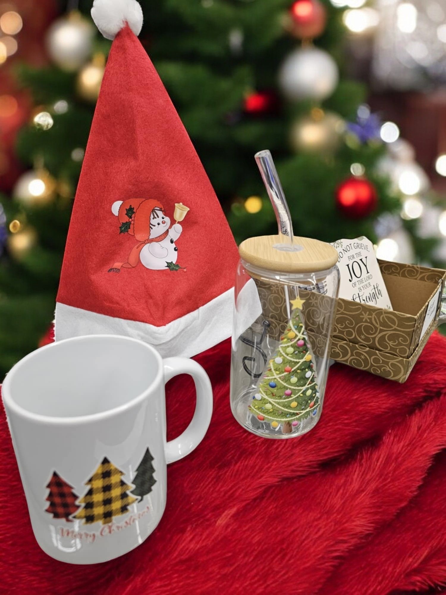 A christmas gift set with a santa hat , a mug , and a glass with a christmas tree on it.