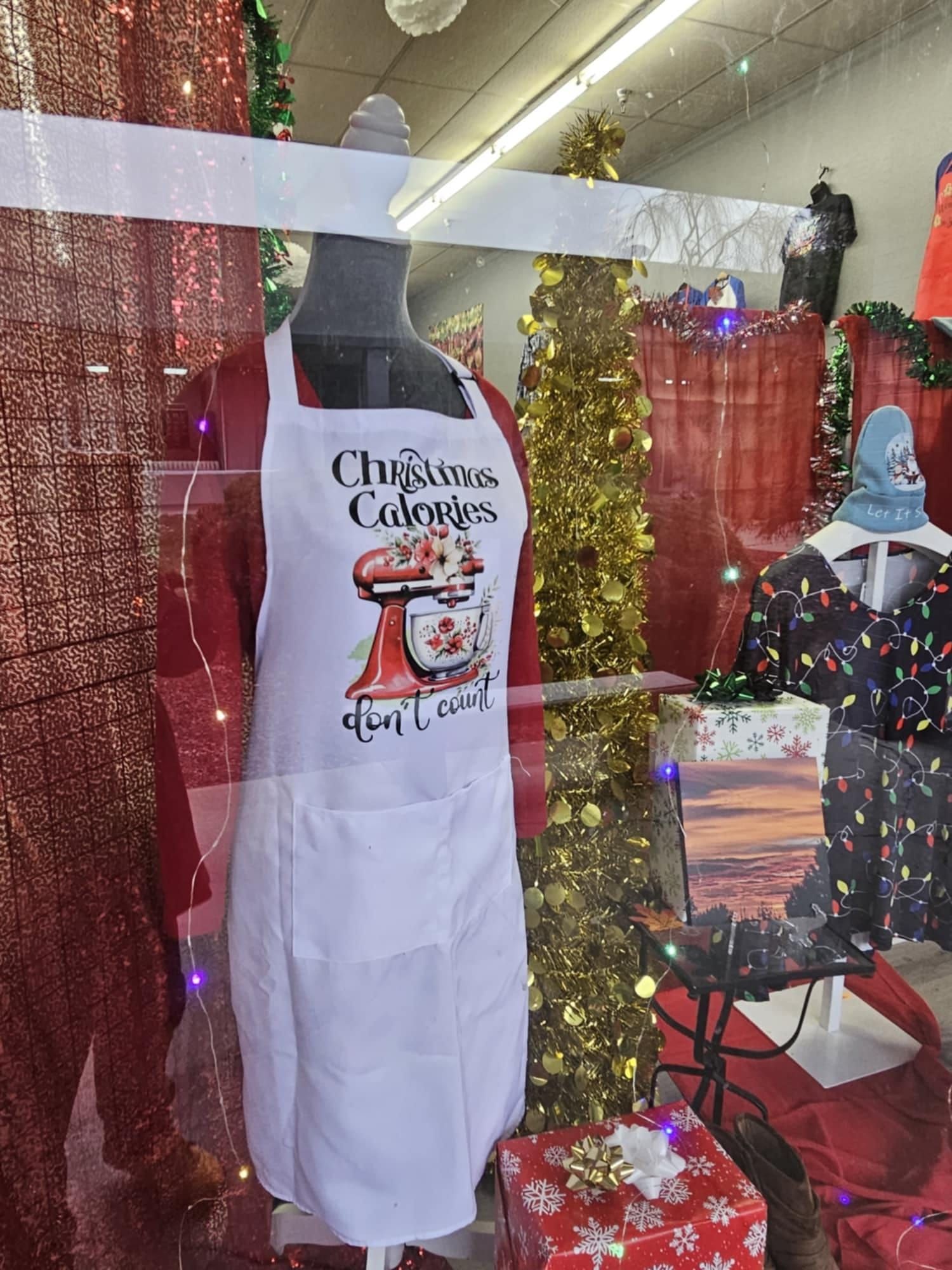 A mannequin is wearing a christmas apron in a store window.
