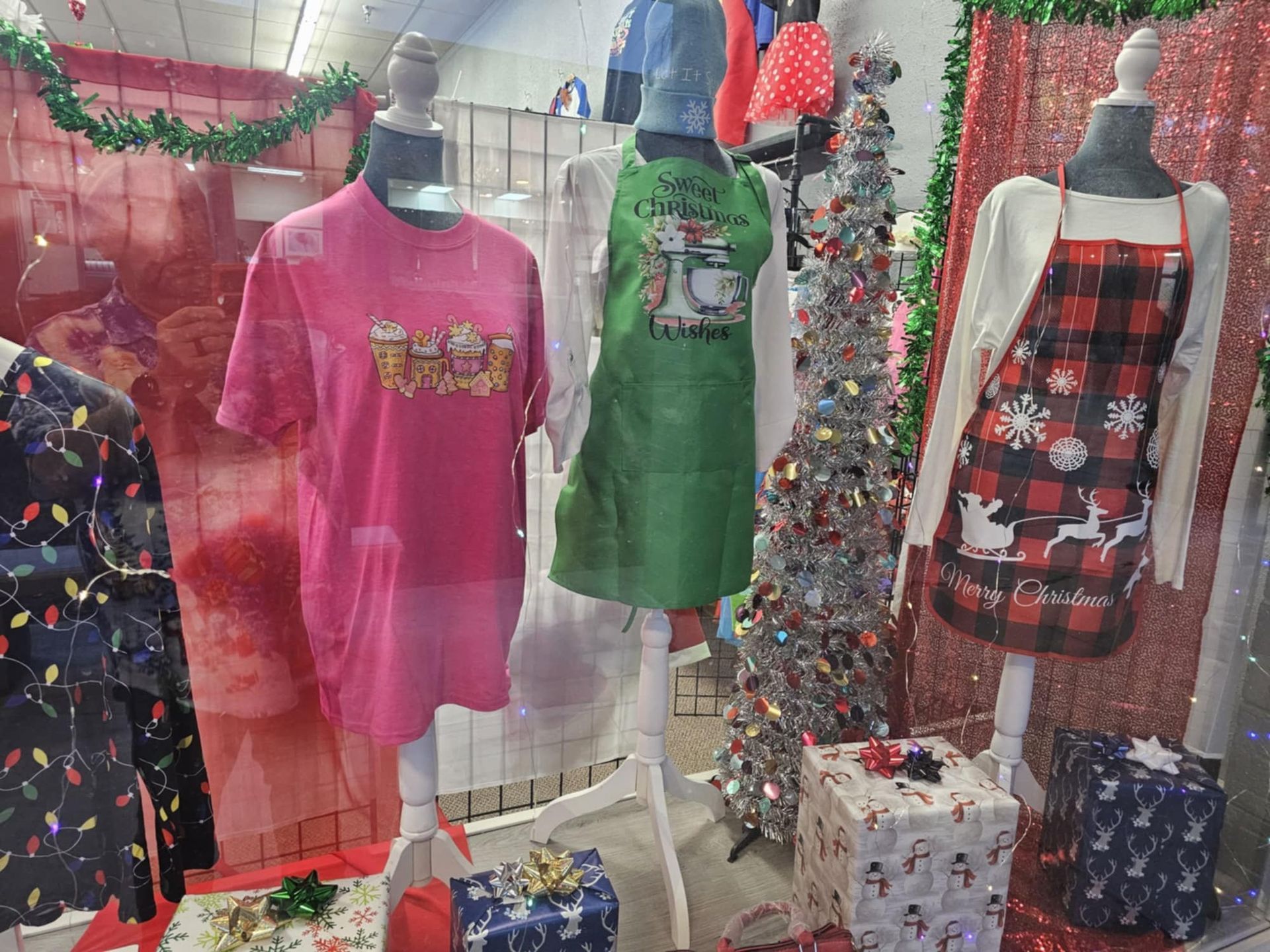 A display of christmas clothes and a christmas tree in a store window.