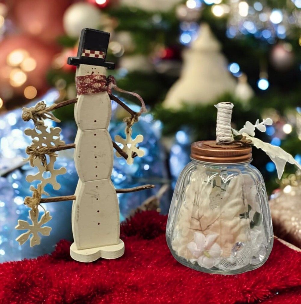 A snowman and a jar of seashells sit on a red blanket in front of a christmas tree