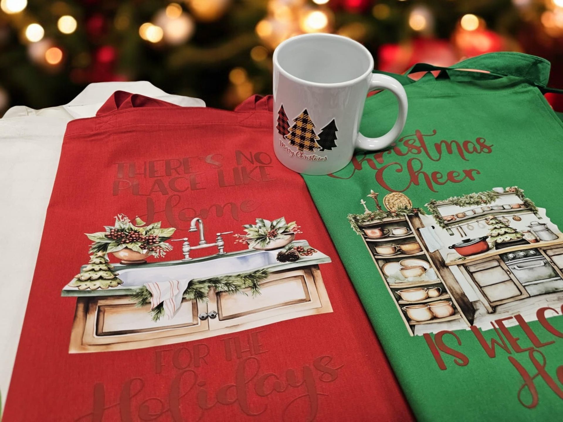 Two christmas shirts and a mug are sitting on a table in front of a christmas tree.
