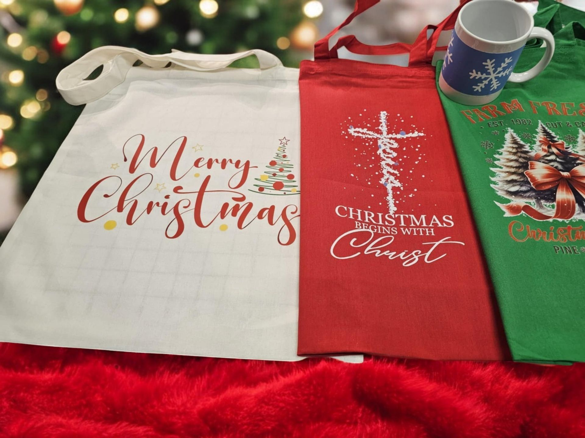 Three christmas shirts are sitting on a red blanket with a christmas tree in the background.