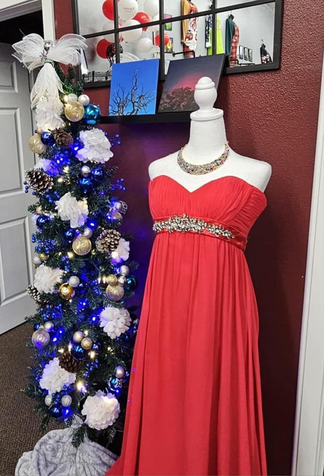 A red dress is on a mannequin in front of a christmas tree