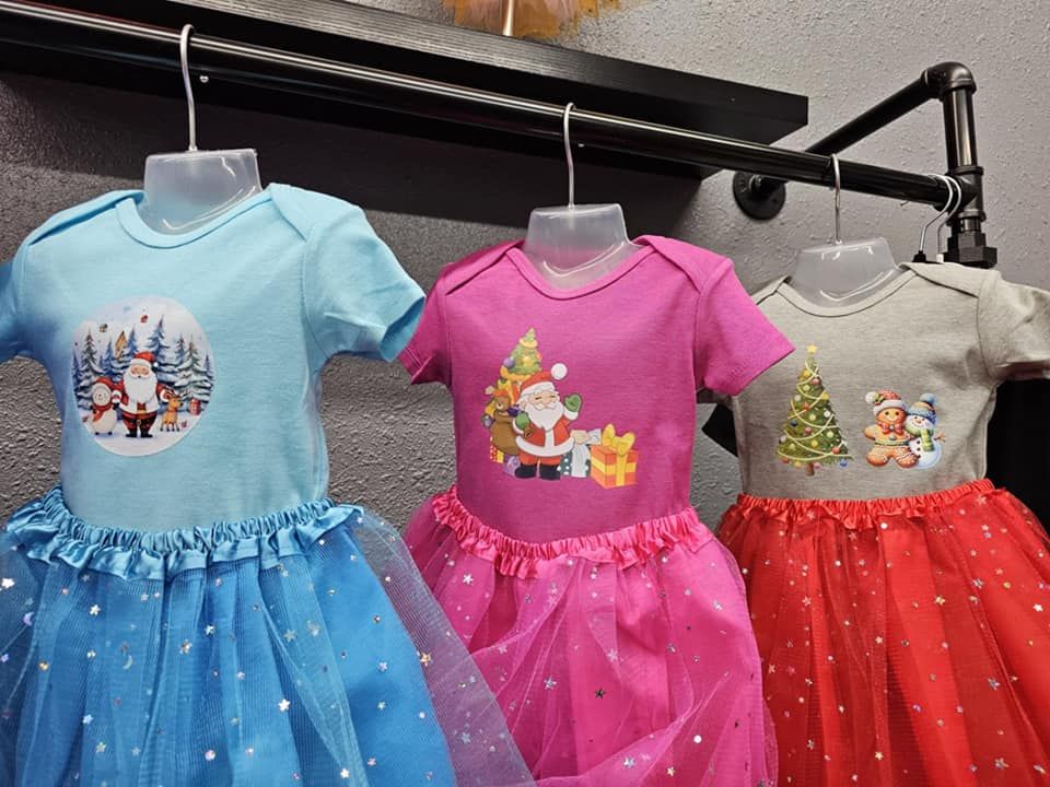 Three baby dresses are hanging on a rack in a store.