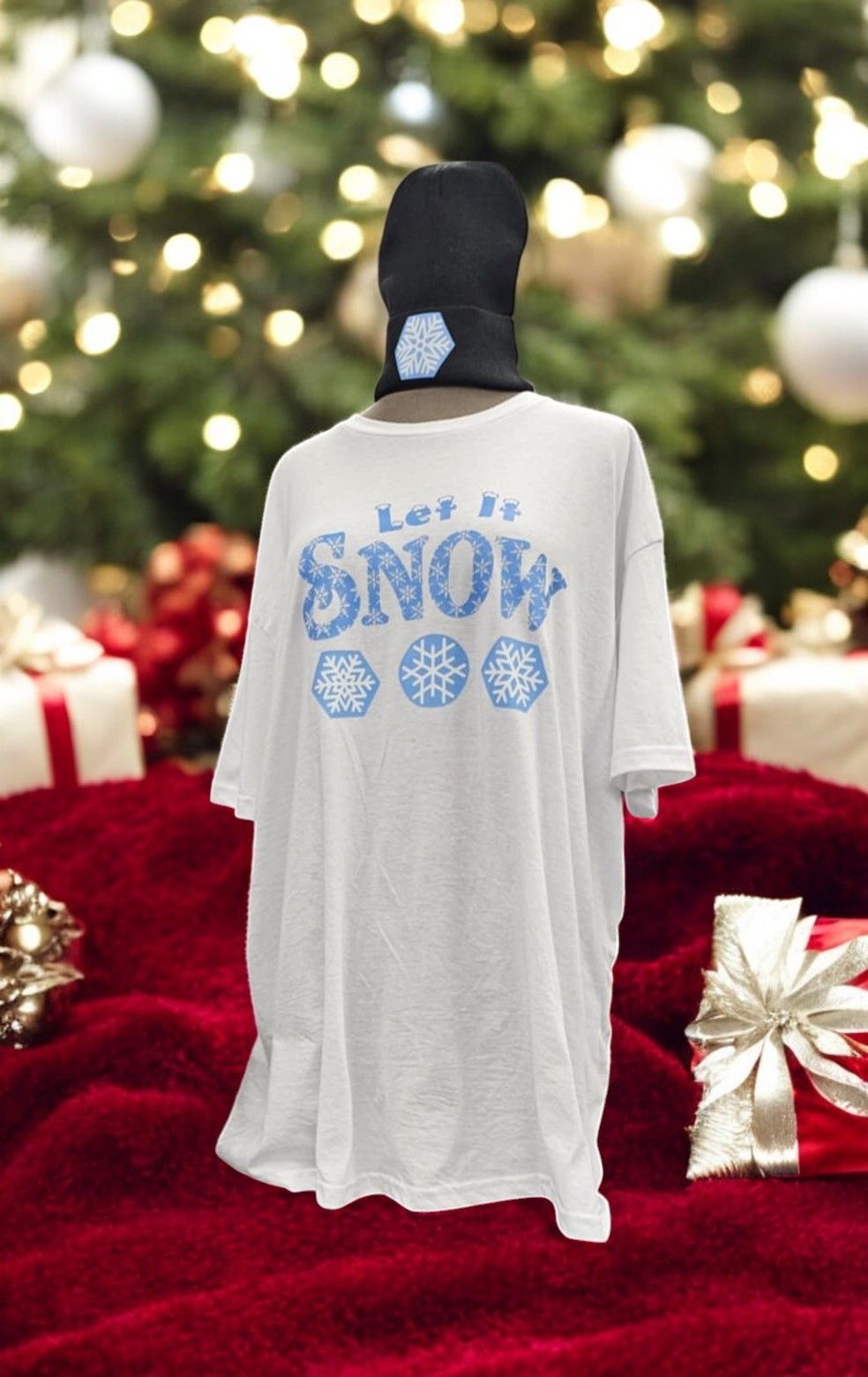 A white t-shirt that says let it snow is on a mannequin in front of a christmas tree.