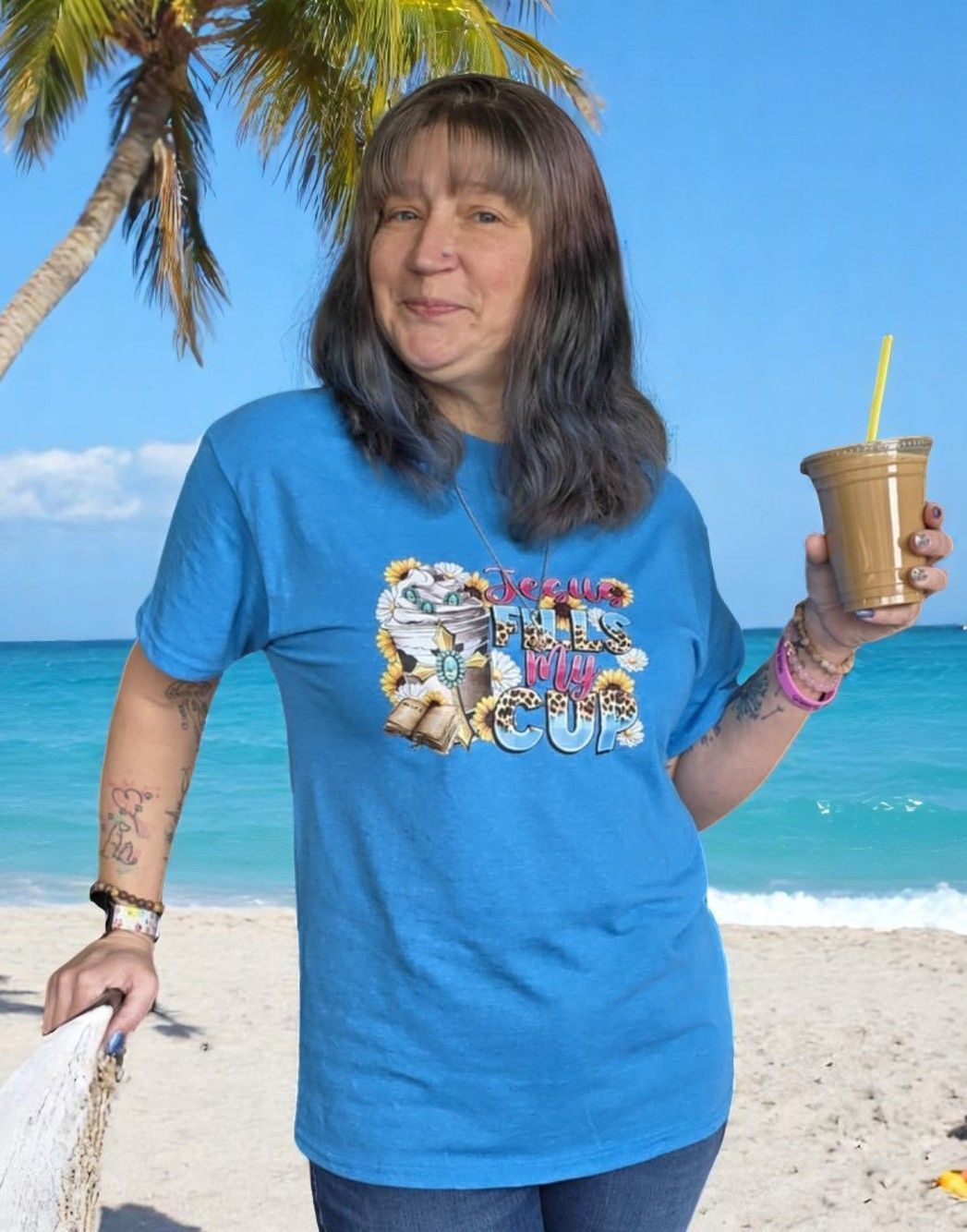 A woman in a blue shirt is holding a drink on the beach