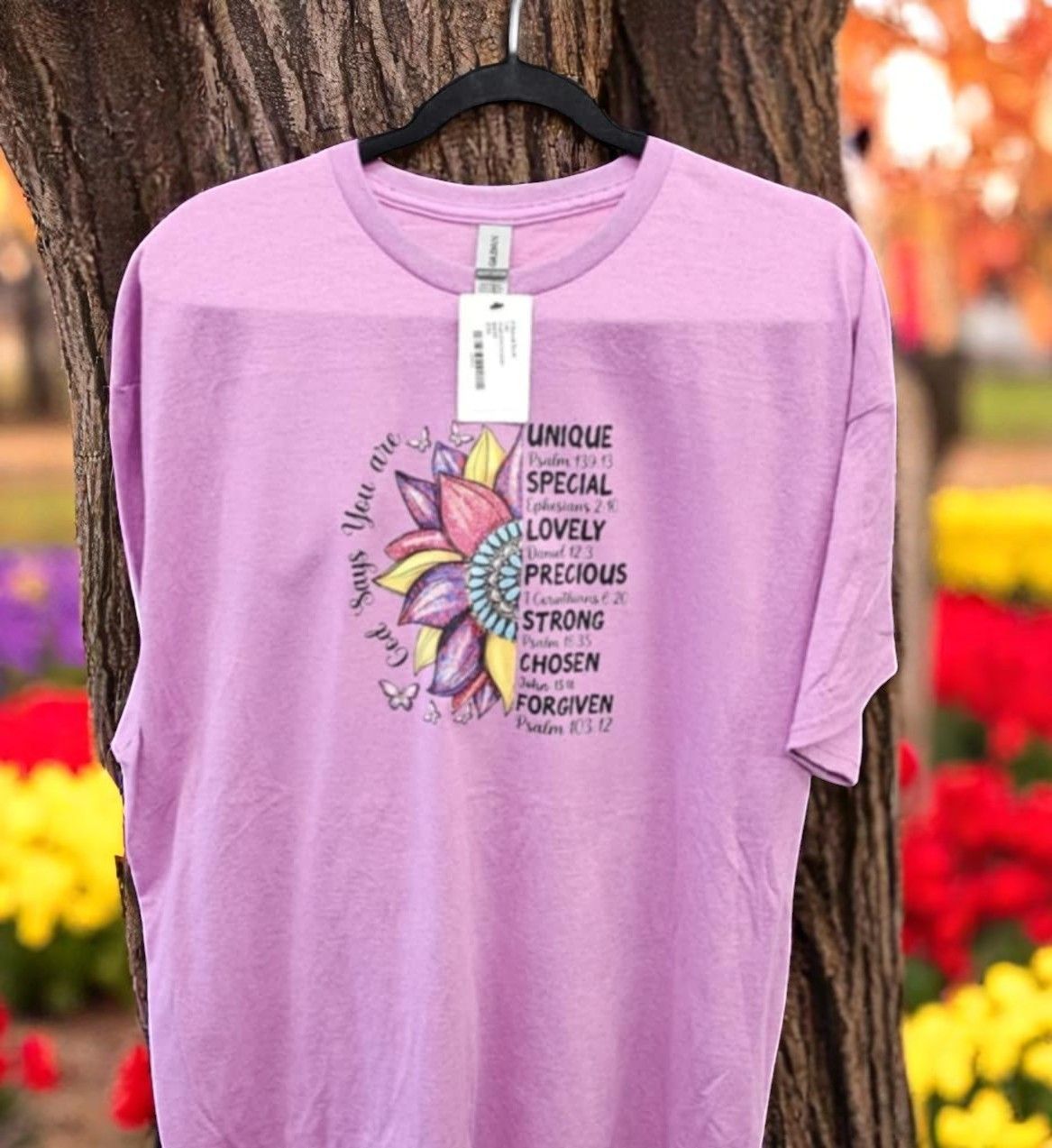 A purple t-shirt with a flower on it is hanging on a tree.