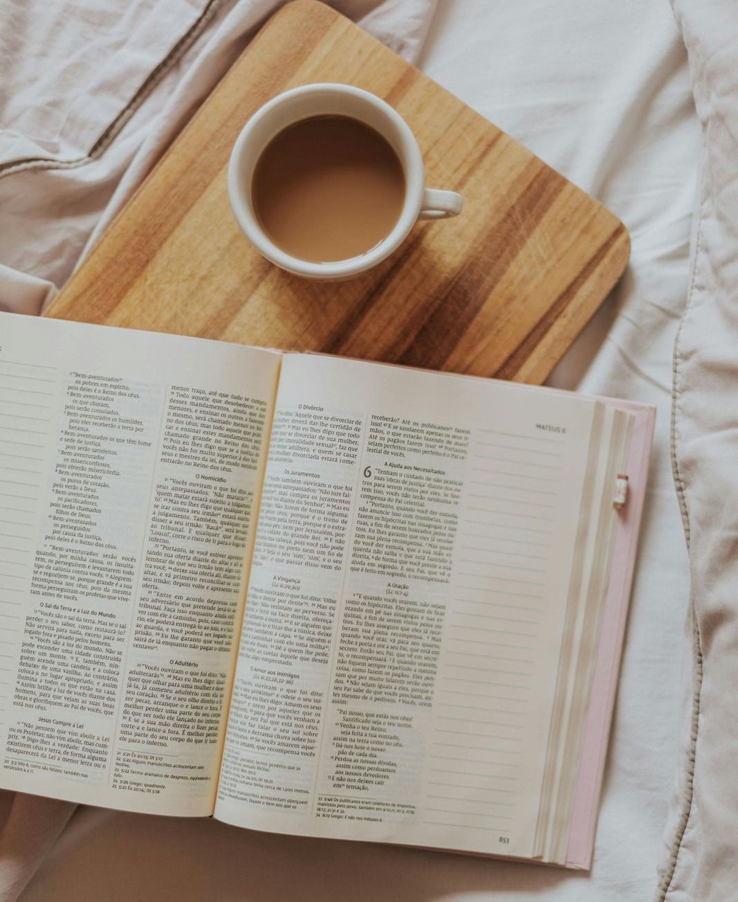 A cup of coffee sits on a wooden cutting board next to an open book