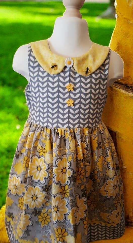 A little girl is wearing a yellow and gray dress on a mannequin.
