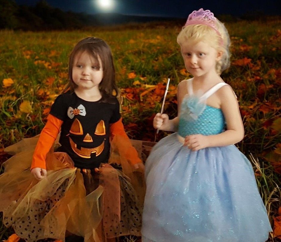 Two little girls in halloween costumes are standing in a field