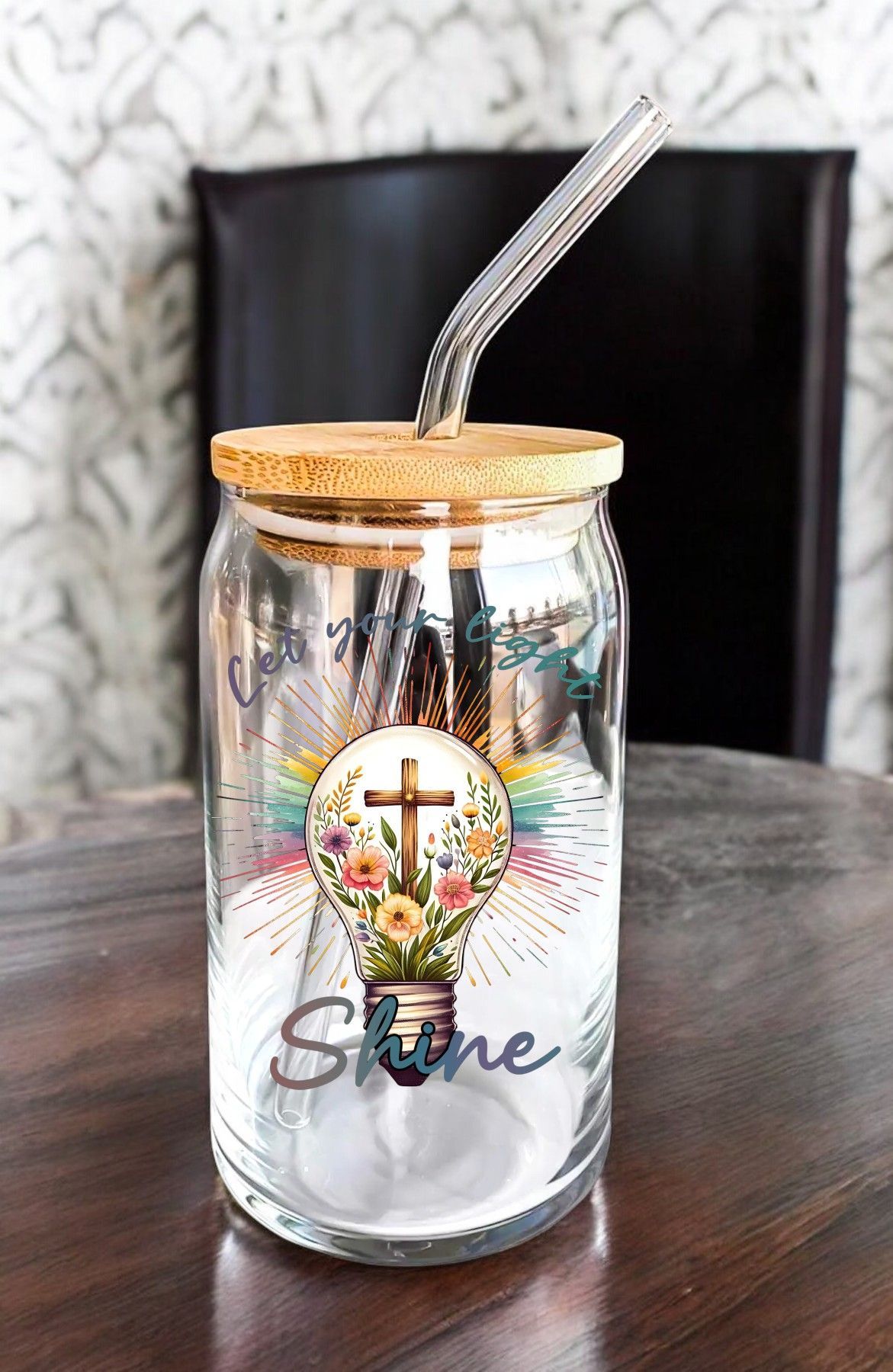 A glass jar with a straw and a light bulb on it is sitting on a wooden table.