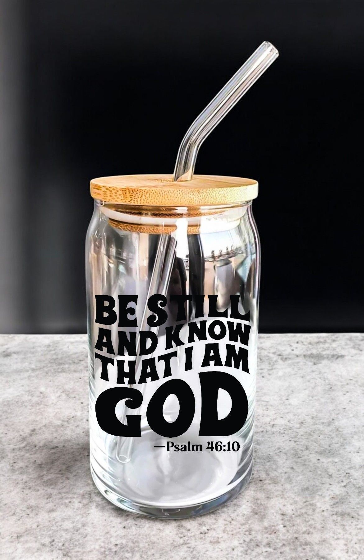 A glass jar with a straw and the words `` be still and know that i am god '' on it.