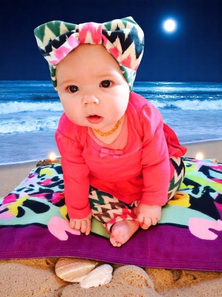 A baby wearing a headband is sitting on a beach towel