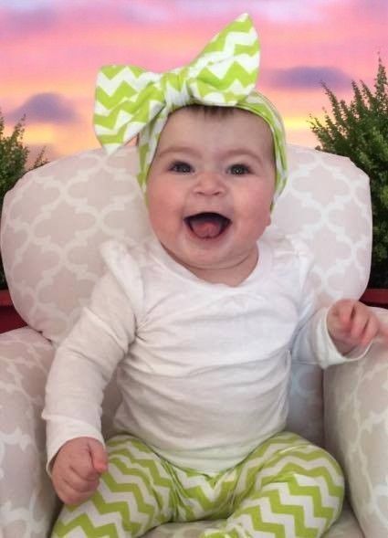 A baby wearing a green and white headband is sitting in a chair