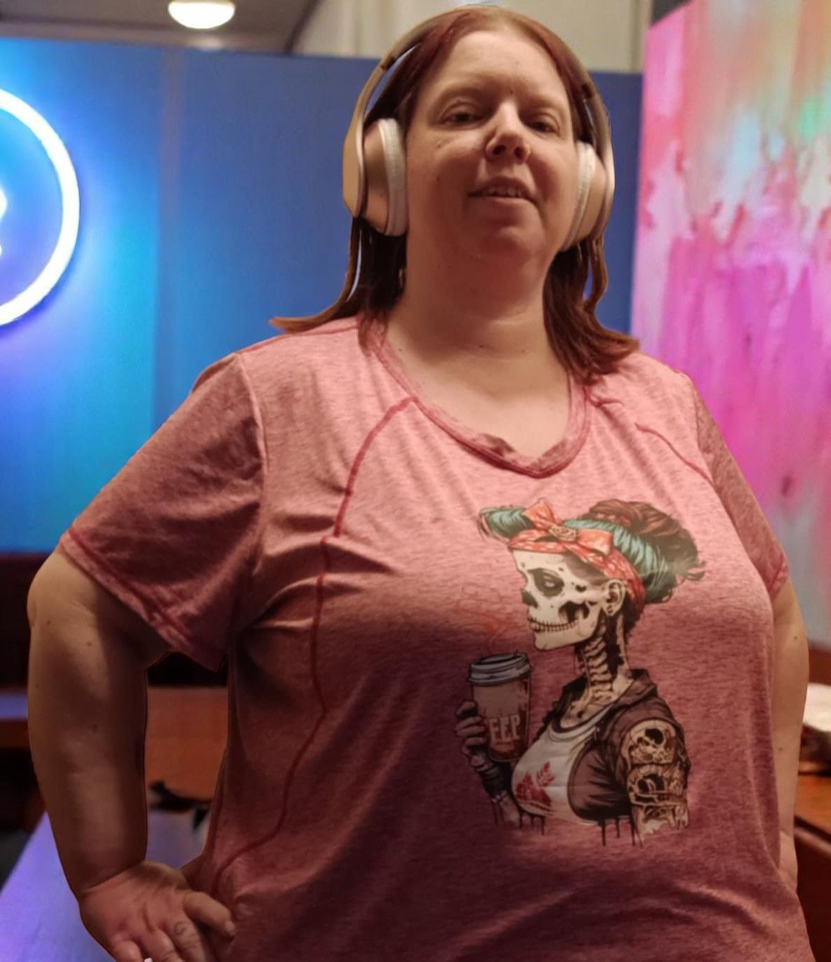 A woman wearing headphones and a pink shirt with a skeleton on it.