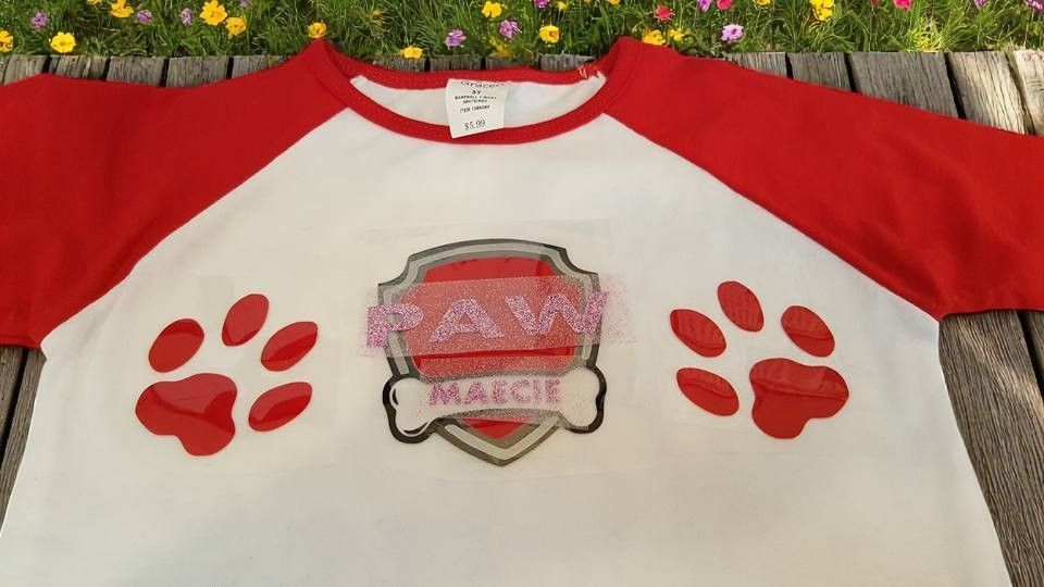 A t-shirt with paw patrol paw prints on it is sitting on a wooden table.