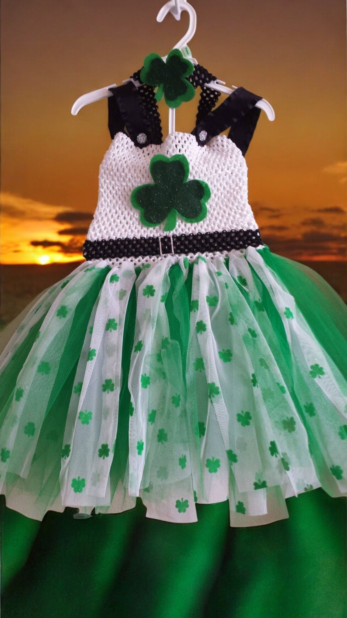 A green and white dress with a shamrock on it is hanging on a hanger.