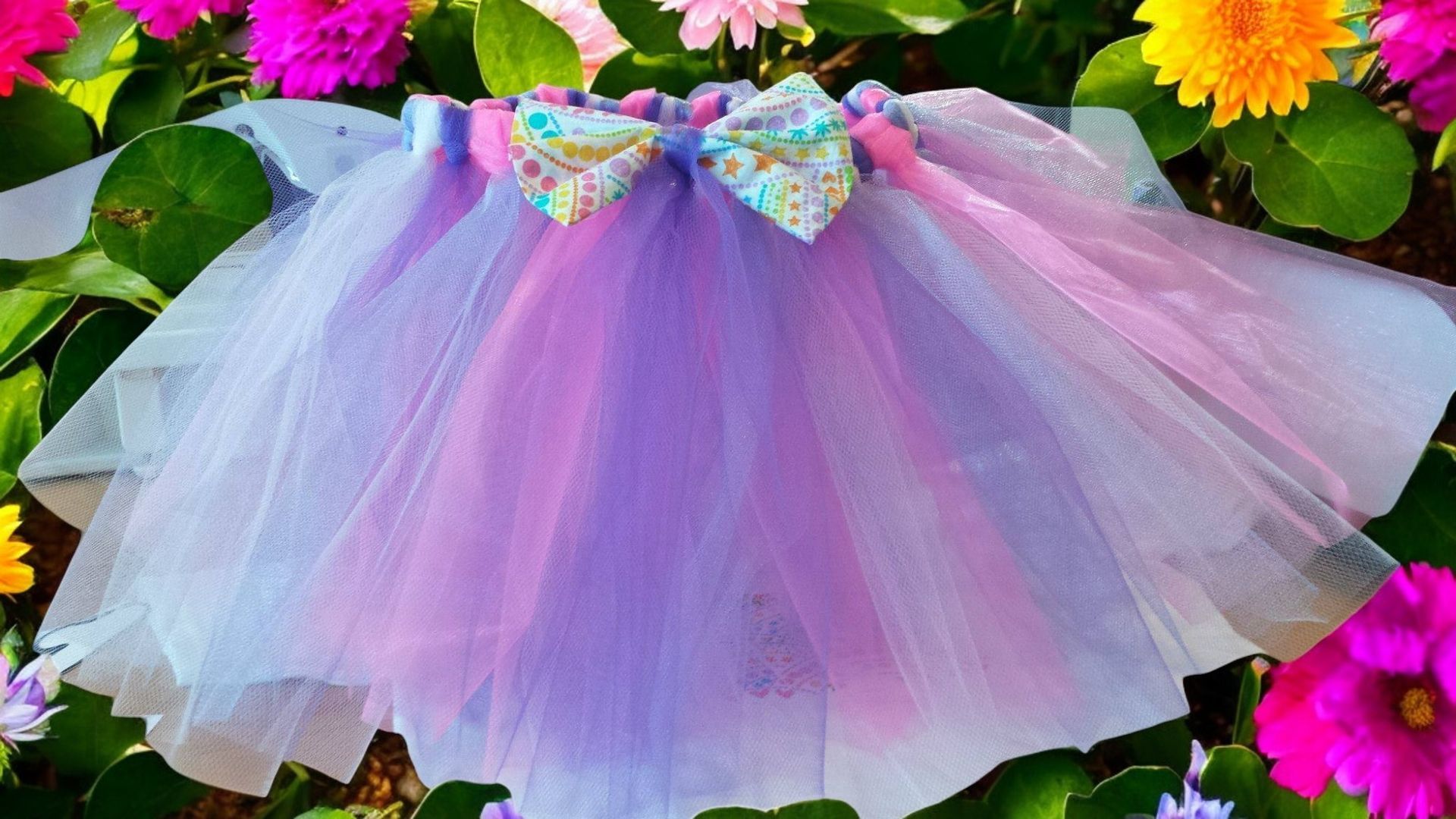 A purple and pink tutu with a bow is surrounded by flowers.