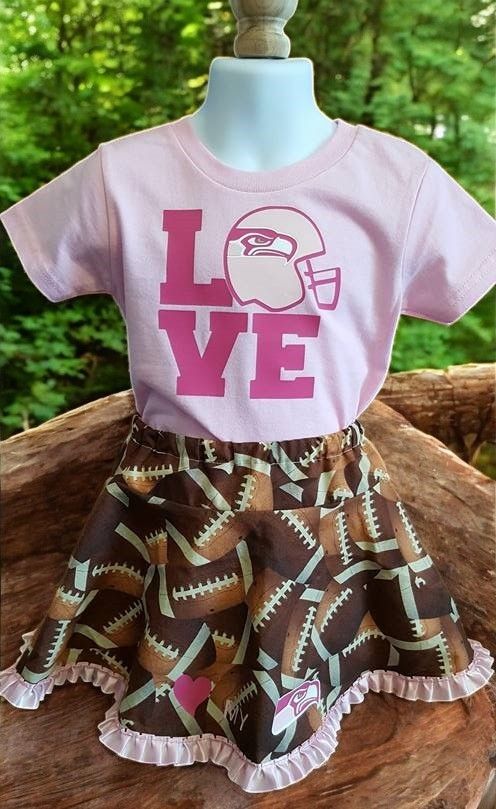 A little girl is wearing a pink shirt that says love and a brown skirt with footballs on it.