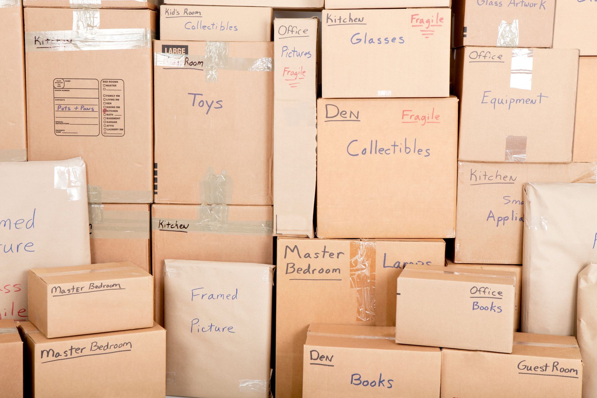Cardboard boxes stacked, labeled with contents like toys, books, and collectibles, ready for a move.