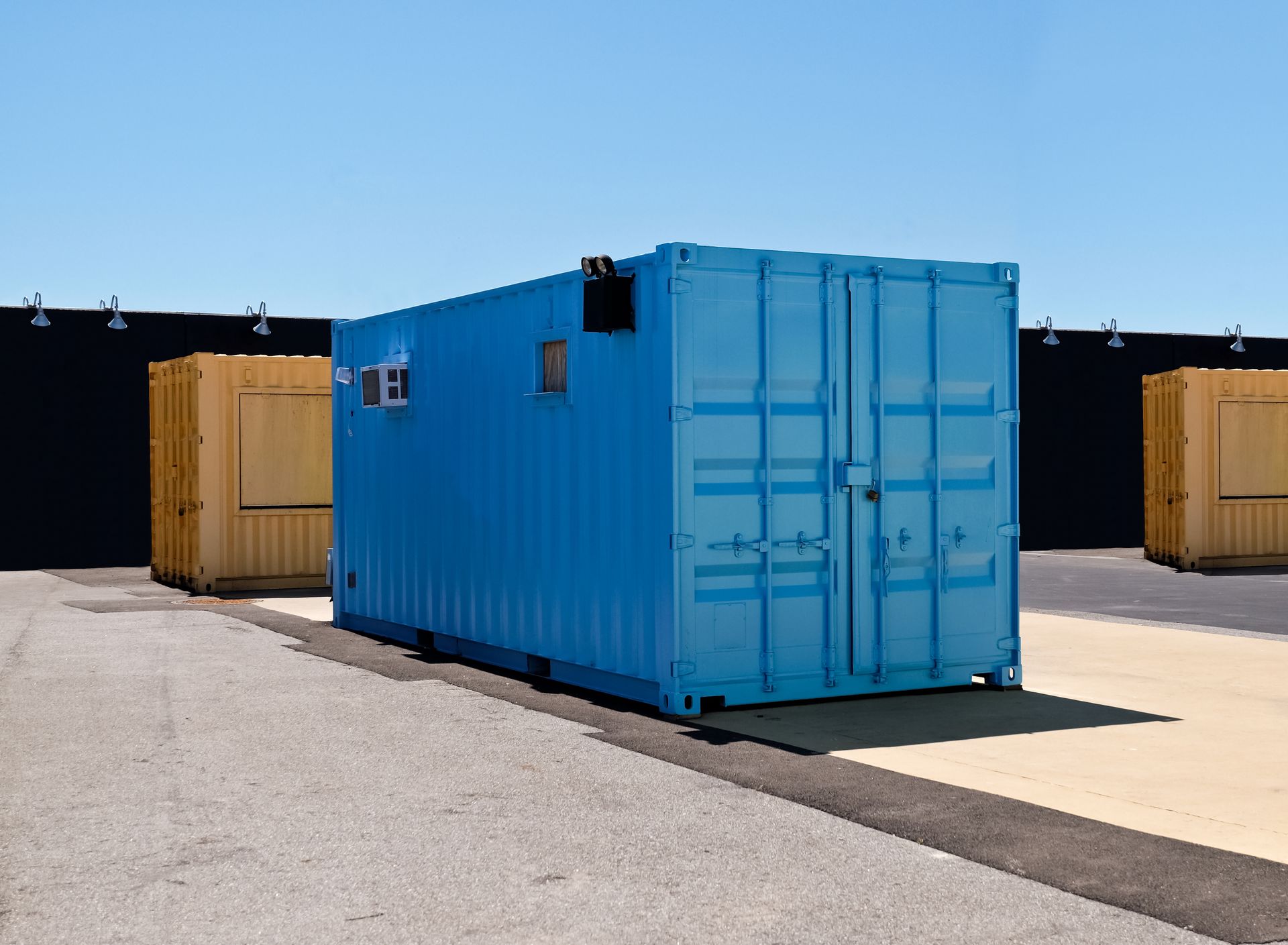 A row of open shipping containers on semi-trucks, connected to a pump on the ground with hoses in a dirt lot.