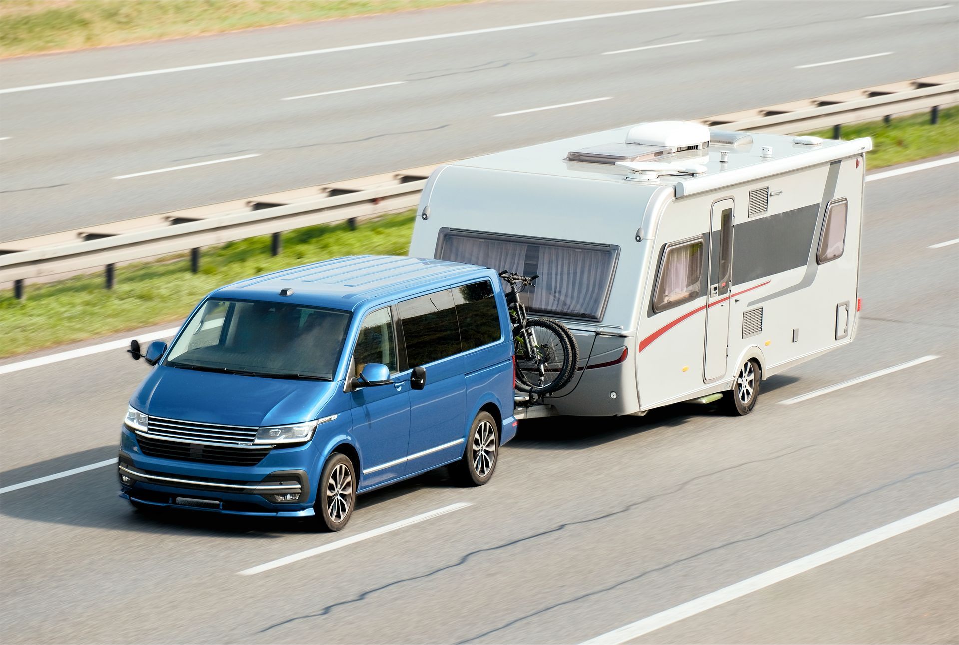 Blue van towing a white and gray camper on a highway.