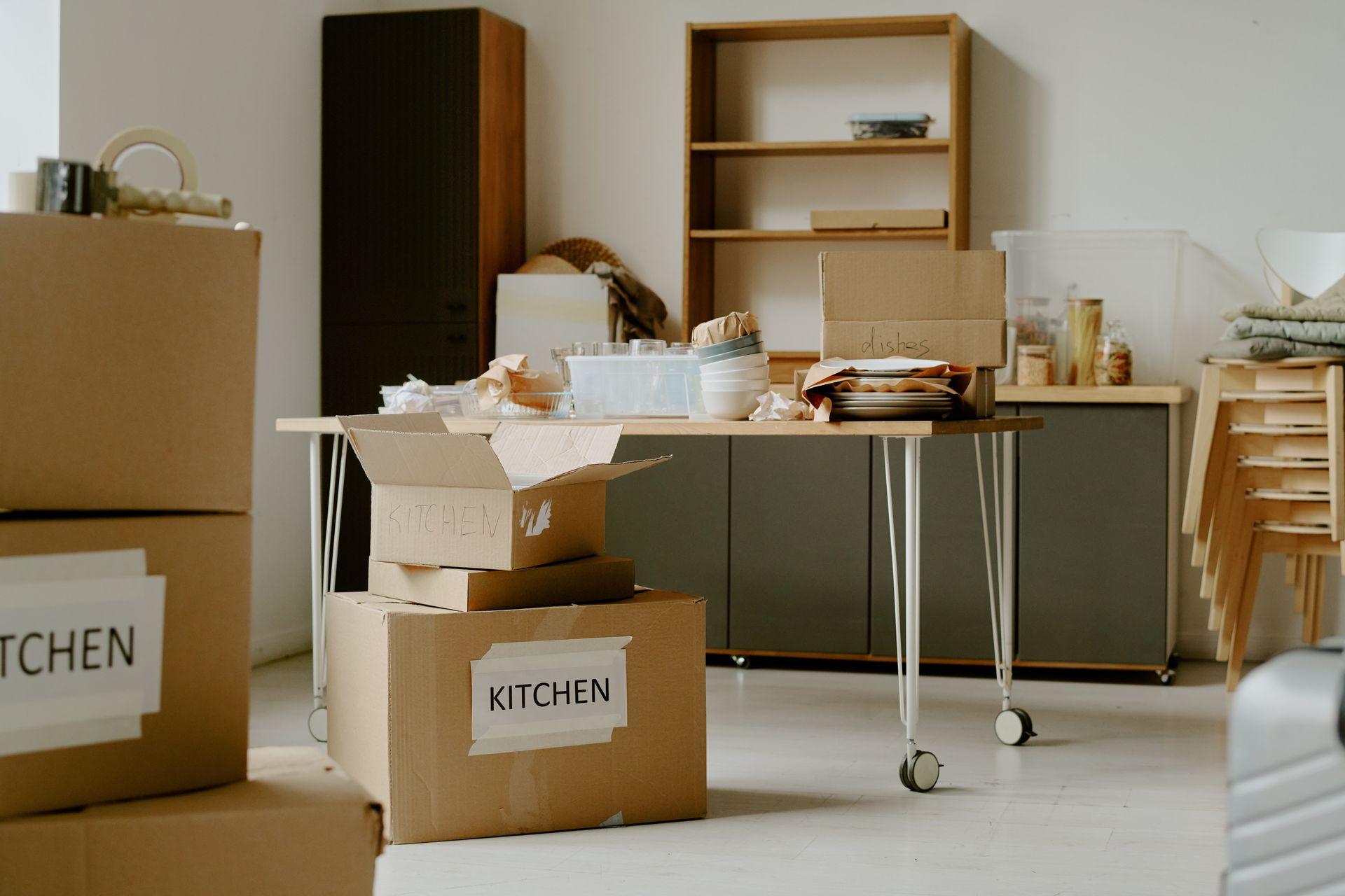 Boxes labeled as KITCHEN in a room, with packed items on a table and shelves, preparing for a move.