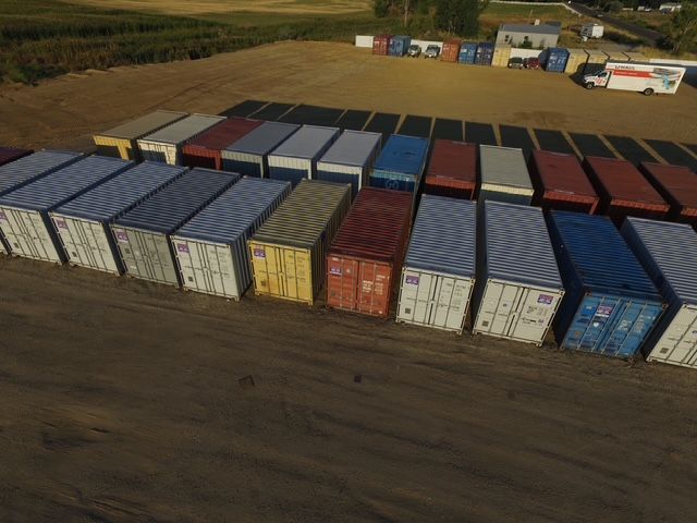White storage shipping containers stacked two levels high next to a white building.