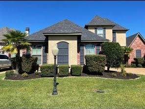 A single-story suburban house with beige stucco, a gray roof, dark shutters, a front garden, and a decorative lamp post.