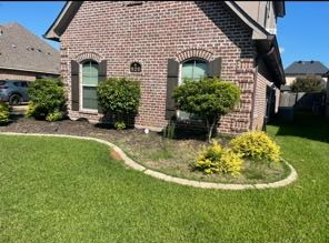 A red brick house with arched windows, brown shutters, and a curved landscaped garden bed in a sunny suburban front yard.