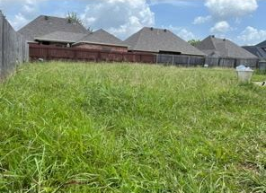 An overgrown, grassy residential backyard enclosed by a wooden fence with neighboring houses in the background.