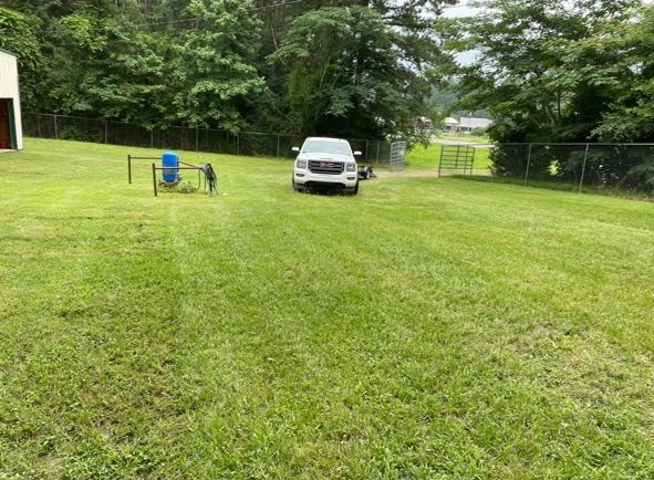 A white GMC pickup truck parked in the center of a large, green, mowed grass yard near a fence and some trees.