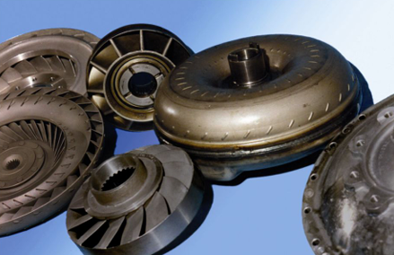 Primer plano de varios convertidores de par automotrices y componentes metálicos sobre un fondo azul.