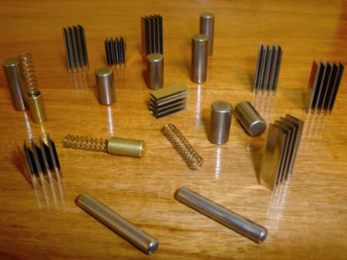 Varios componentes metálicos, incluidos pasadores, cilindros y disipadores de calor, dispuestos sobre una madera.