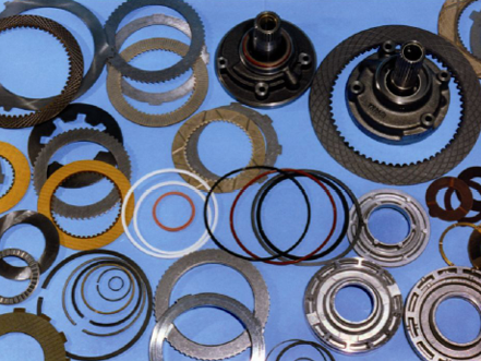 Piezas de transmisión dispuestas sobre una superficie azul, incluidas placas de metal, sellos y otros componentes.