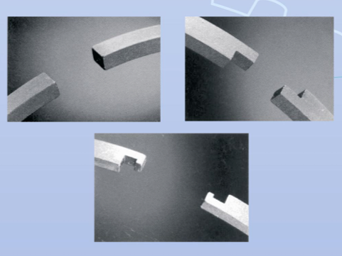 Tres piezas de metal gris con muescas y formas variadas, sobre un fondo oscuro.